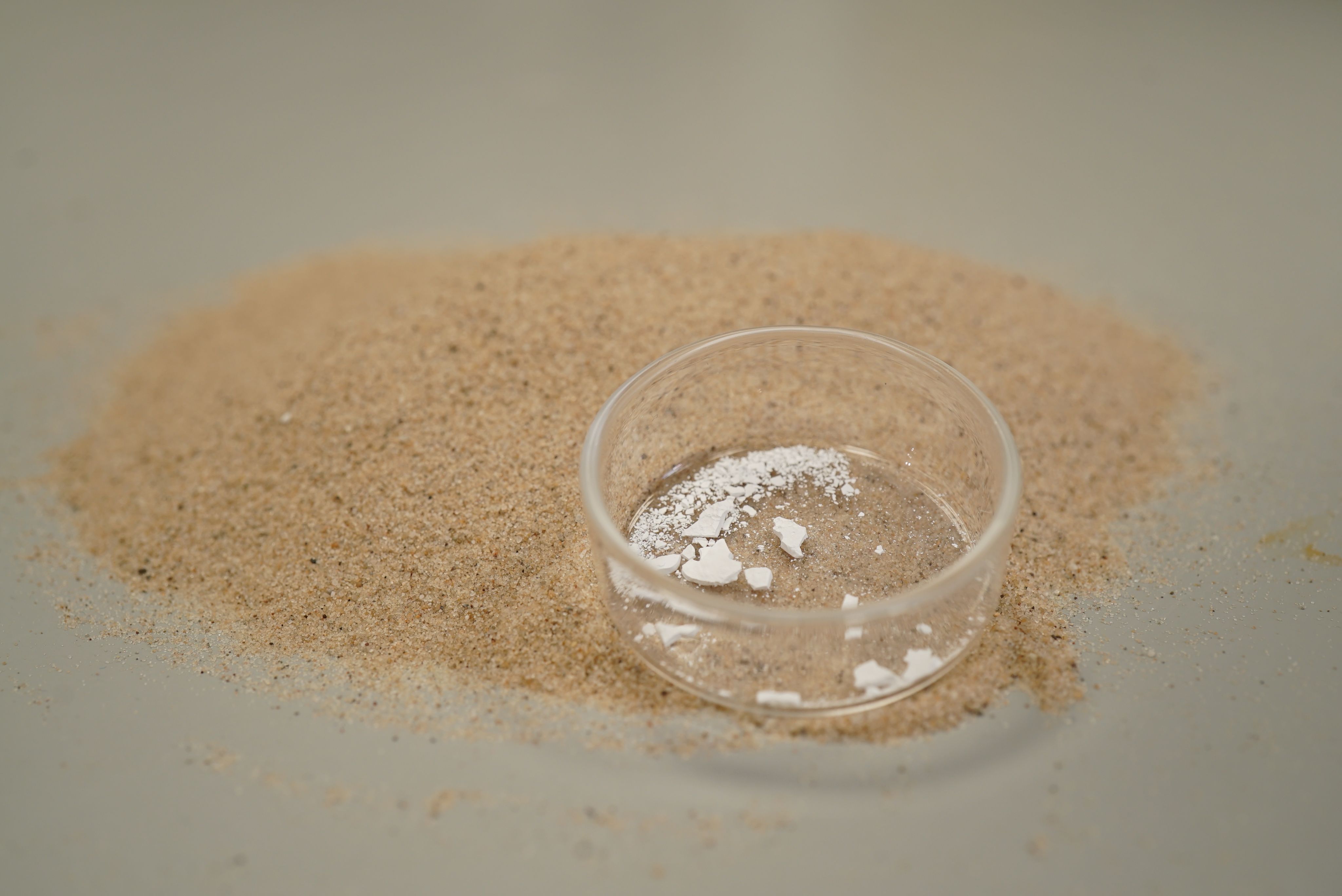 A petri dish with white powder sits on a small pile of sand