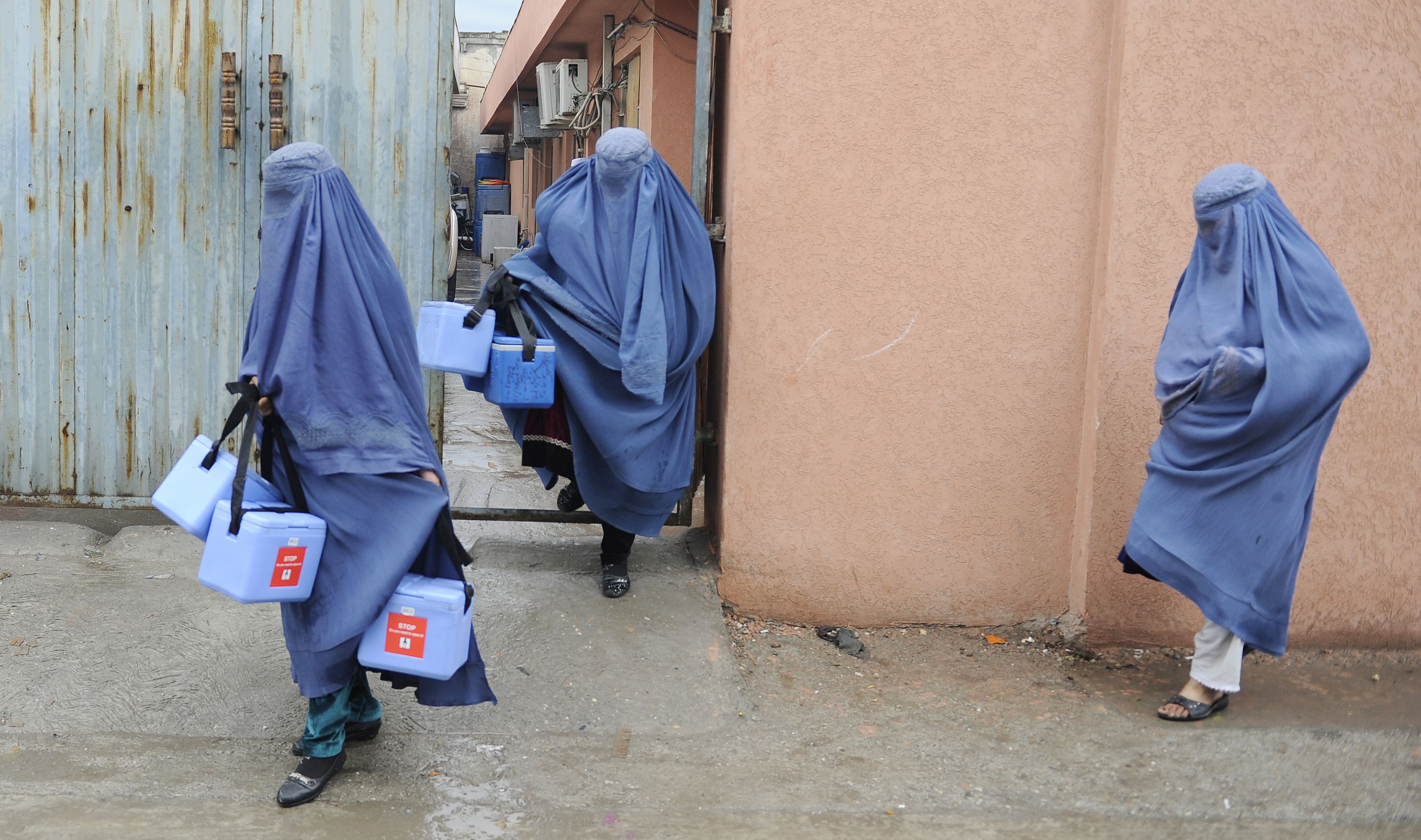 Women wearing burkhas carry frozen medical boxes
